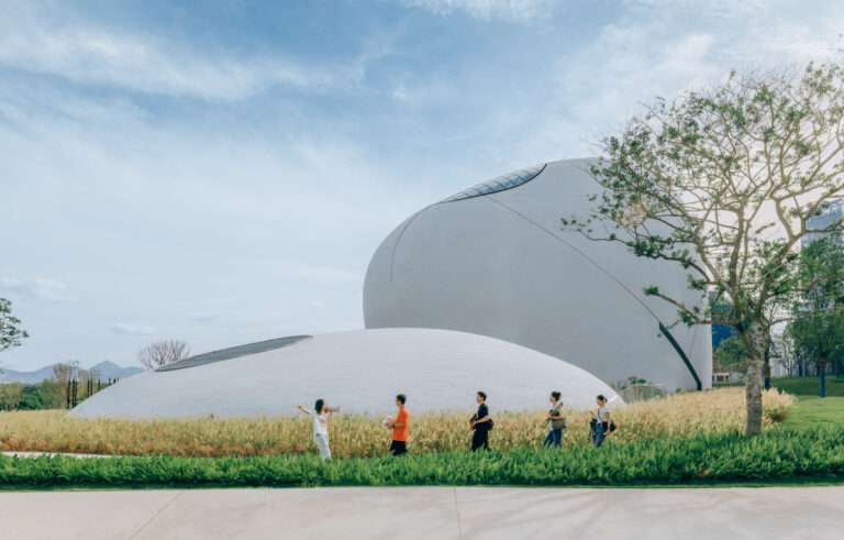 Pedestrians walk along a landscaped path in front of organic curved white granite museum structures.