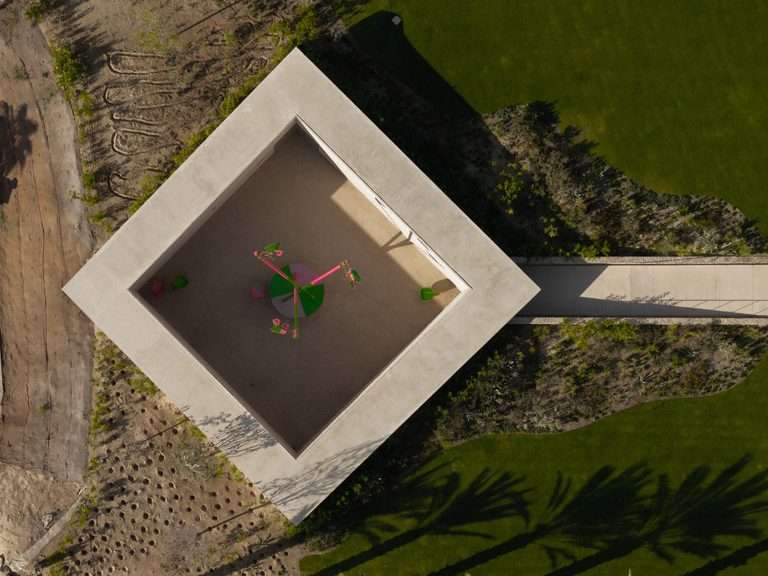 Aerial view looking directly down at a square concrete gallery structure rotated forty-five degrees within surrounding landscape.