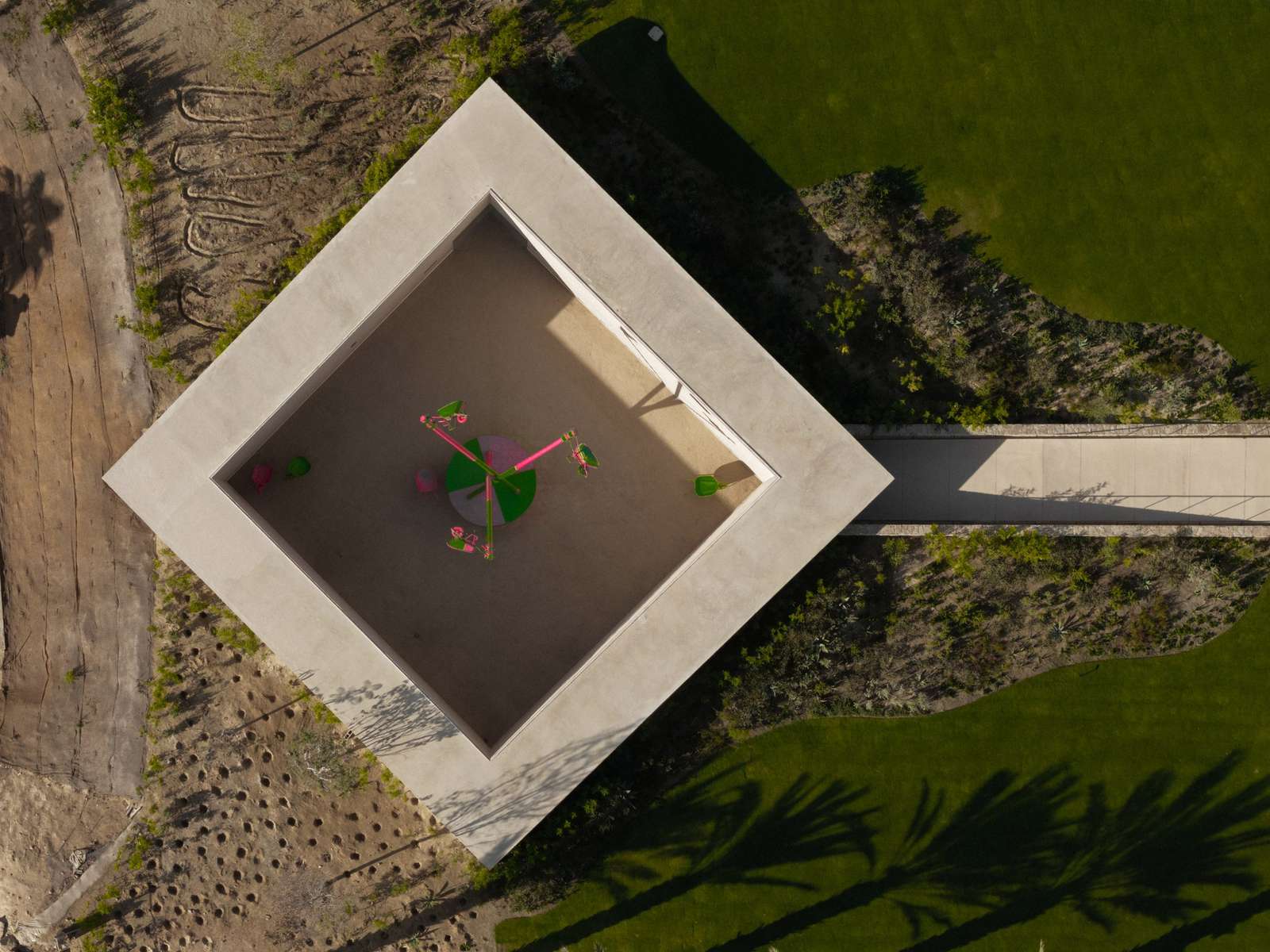 Aerial view looking directly down at a square concrete gallery structure rotated forty-five degrees within surrounding landscape.