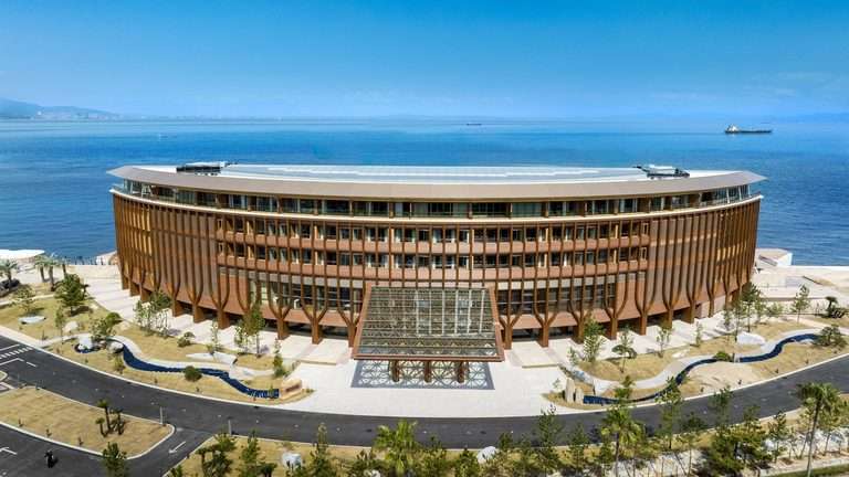 High-angle view of D-shaped wooden hotel building along coastline with entrance canopy.