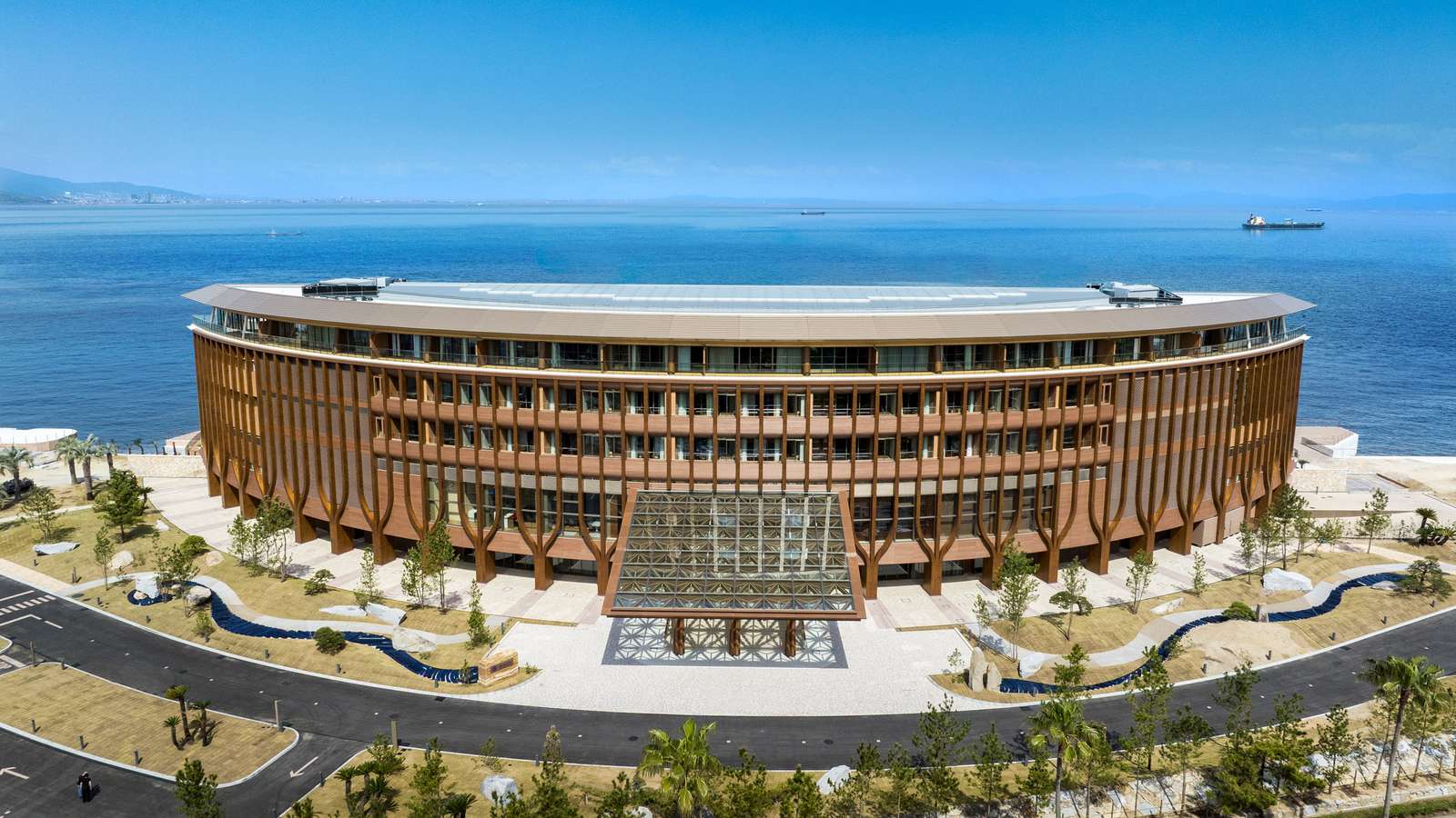 High-angle view of D-shaped wooden hotel building along coastline with entrance canopy.