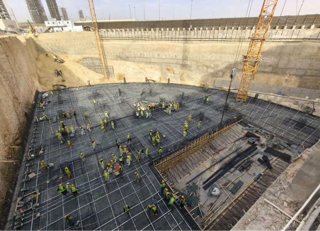 Top-down view of an excavated construction pit with rebar grids and workers on site.