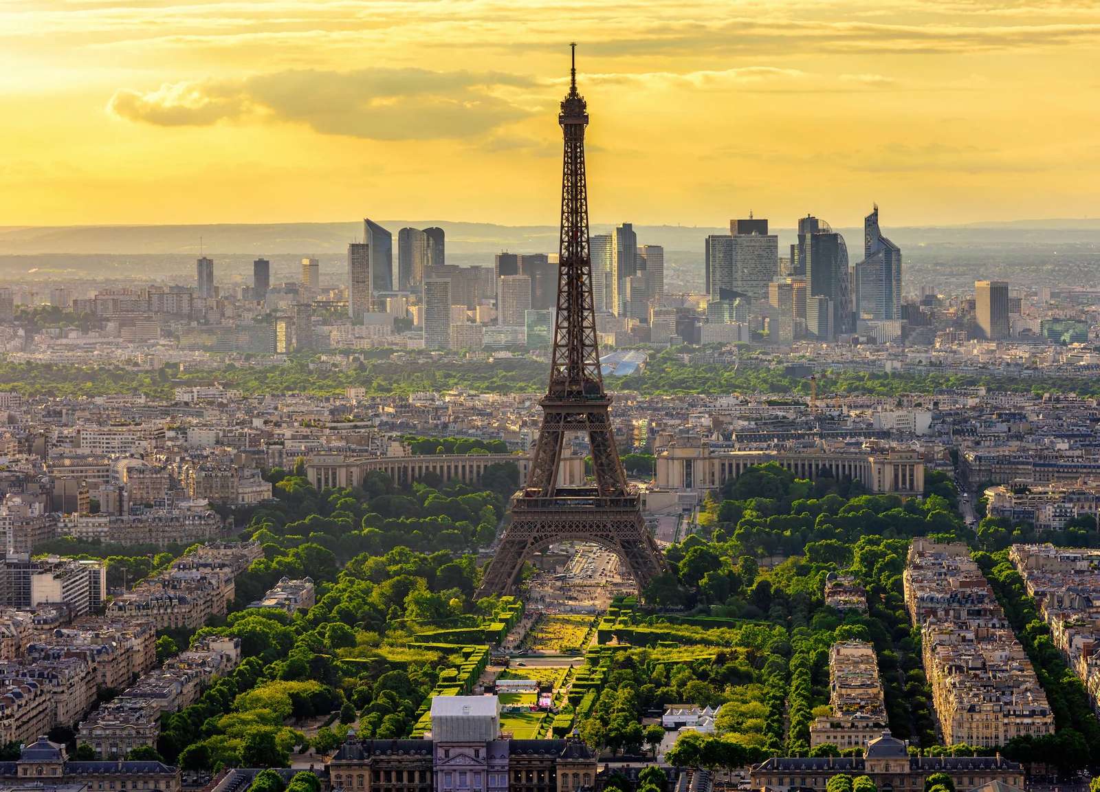High-angle aerial view of the Eiffel Tower leading toward the modern high-rise district in Paris.