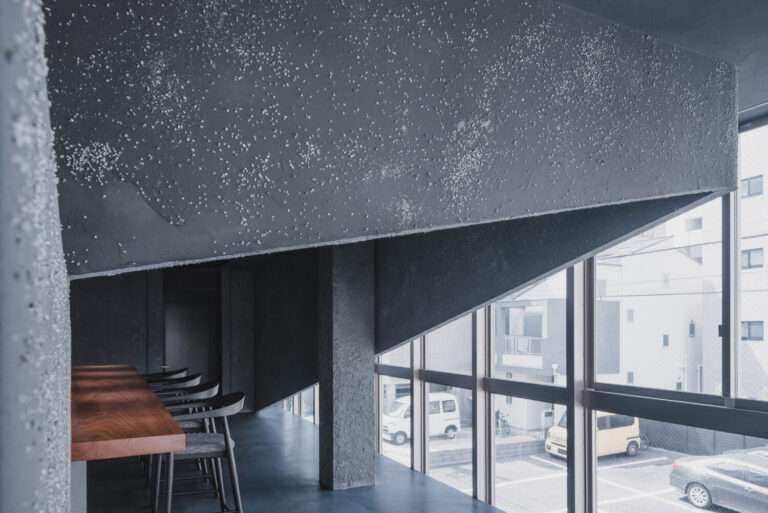 Interior dining space featuring dark textured plaster walls, timber counter, and full-height exterior window wall.