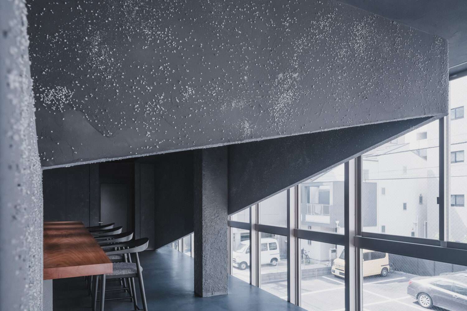 Interior dining space featuring dark textured plaster walls, timber counter, and full-height exterior window wall.