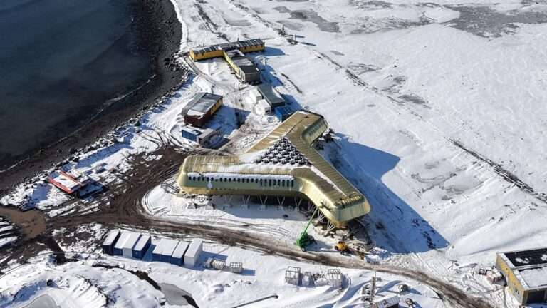 High-angle view of a golden three-winged building near a snow-covered shoreline and dark ocean water.