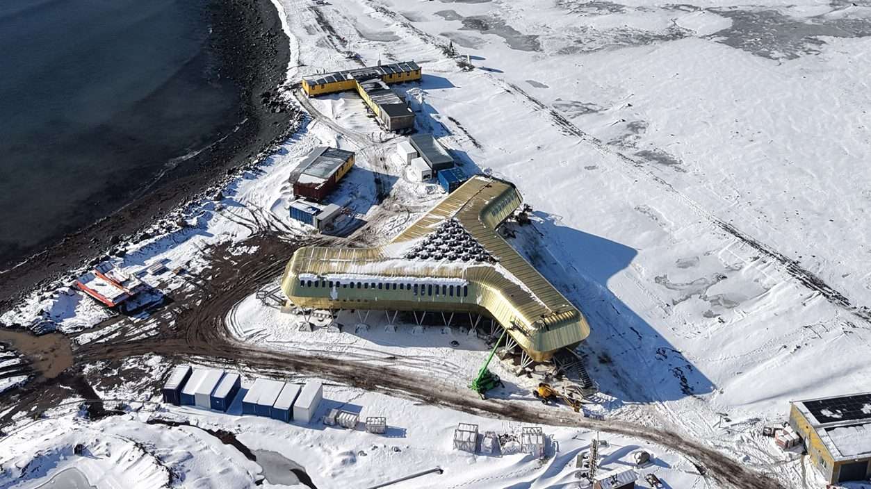 High-angle view of a golden three-winged building near a snow-covered shoreline and dark ocean water.
