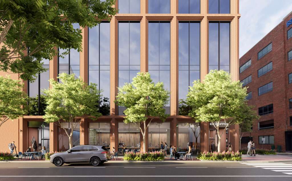 Street-level view of a brick building facade with large glass windows, trees, and pedestrian activity.