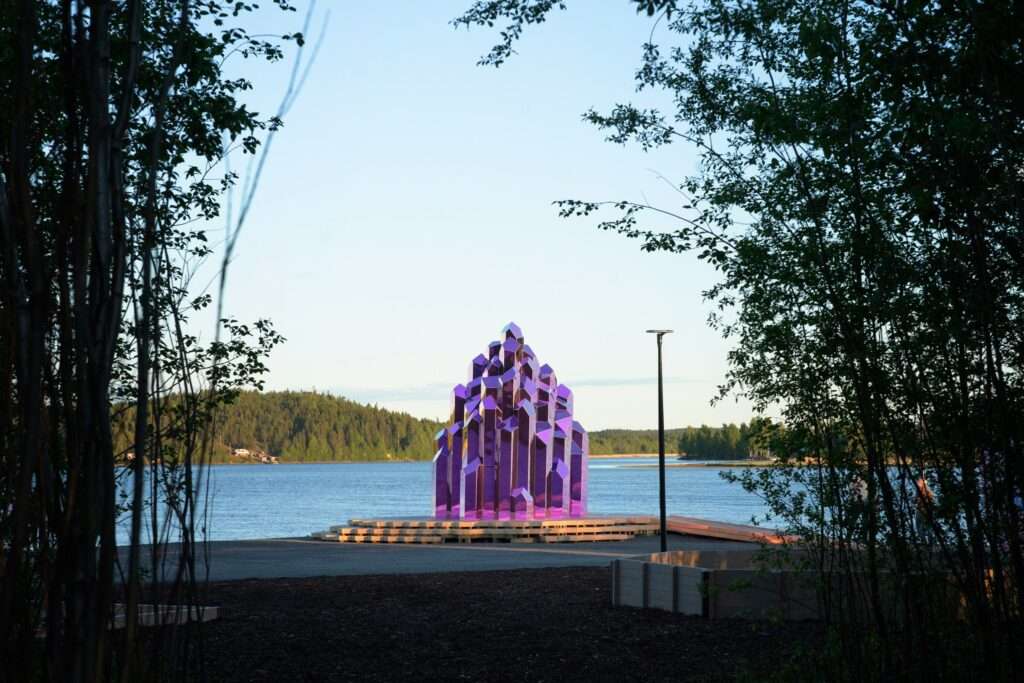 Distanced view of a pink crystal pavilion near a river framed by trees