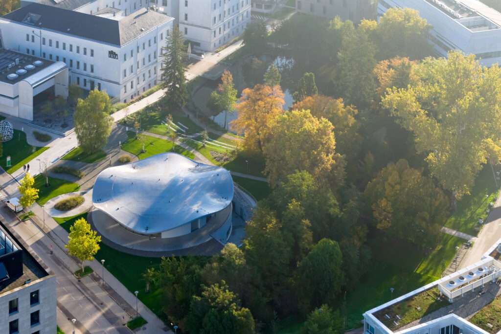 High-angle view showing a circular pavilion roof set within campus parkland and surrounding buildings