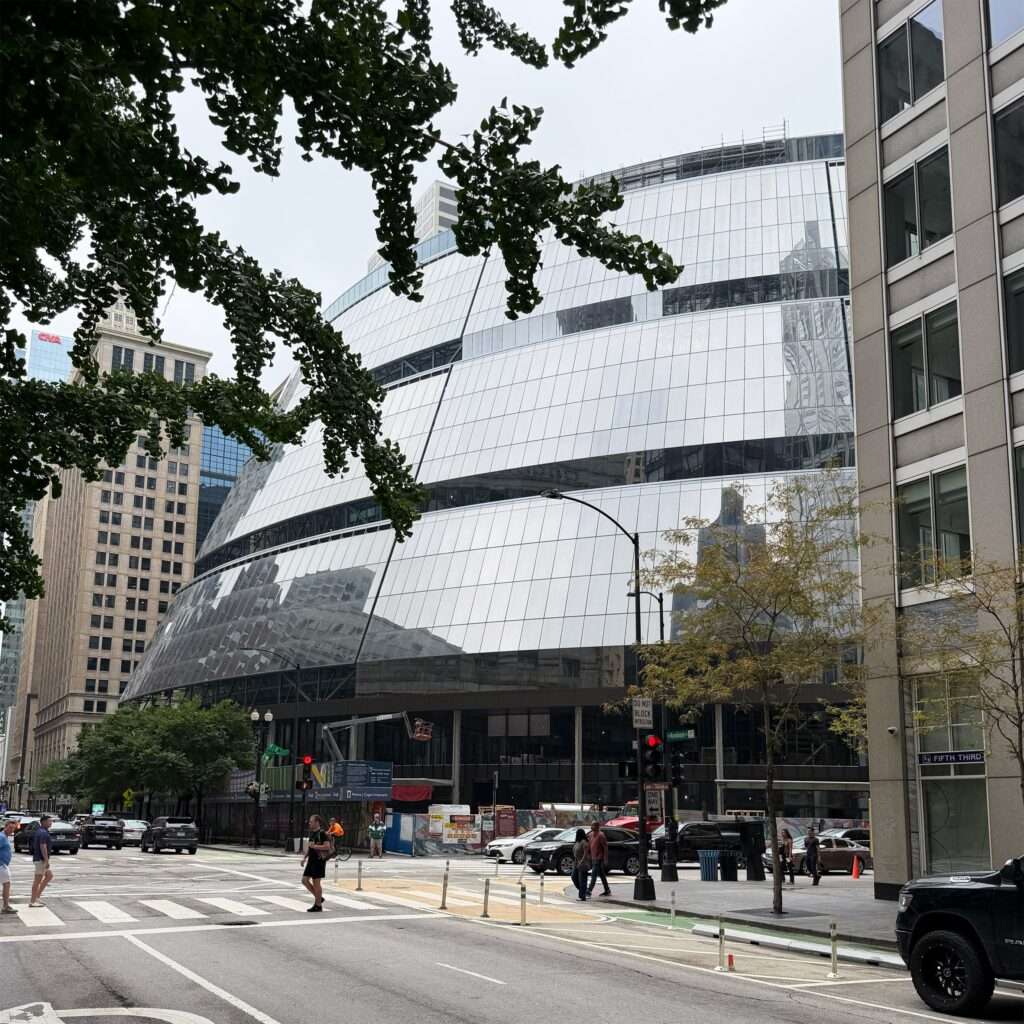 View of the curved glass facade of Thompson Center framed by tree branches and surrounding high-rises.