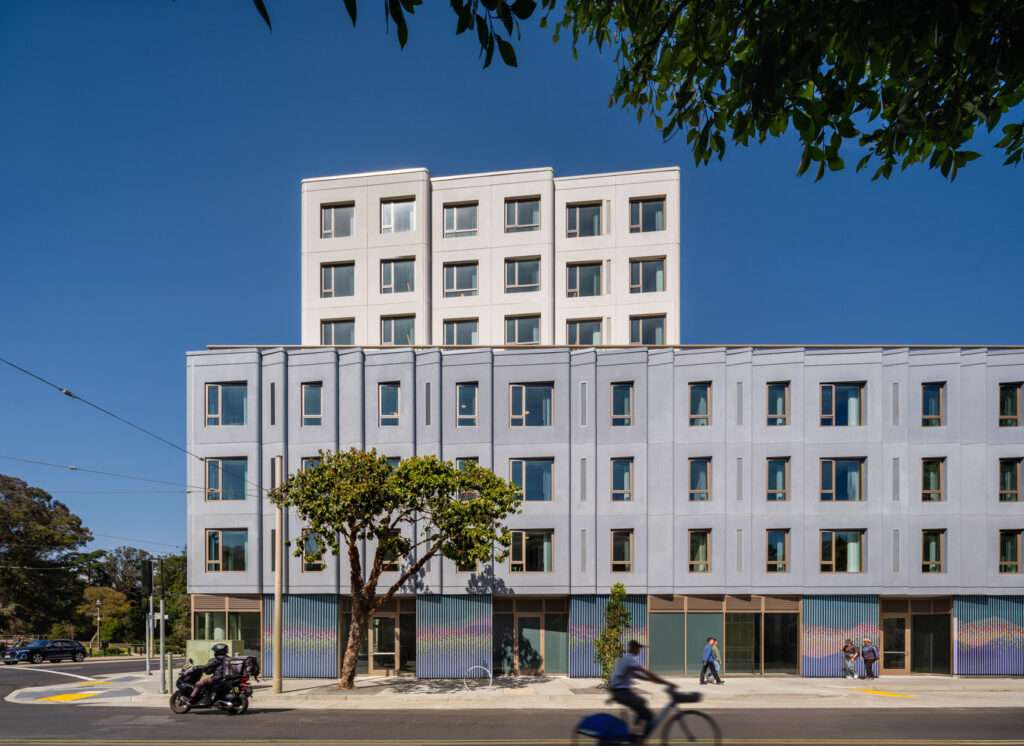 Street-level elevation displaying modular concrete facade panels, fenestration, and ground-floor commercial storefronts.