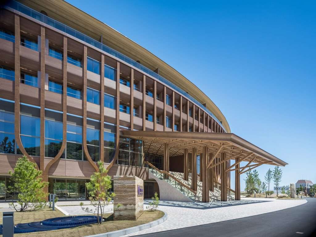 Curved hotel facade with timber-clad columns and expansive wood entrance canopy over wide stairs.