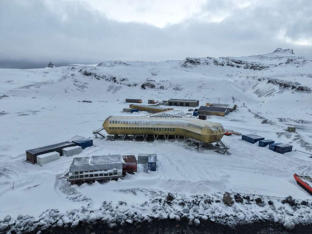 Ground-level view of a elevated golden modular station under an overcast Antarctic sky.