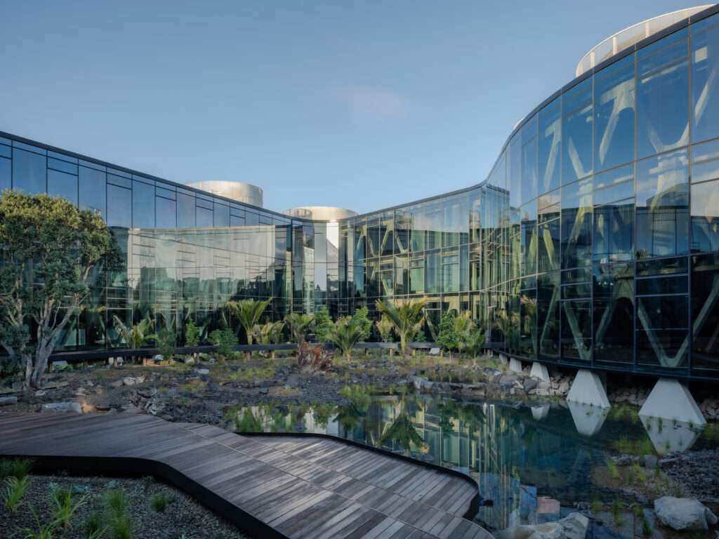 Curved glass facade overlooking an inner courtyard with a wetland pond, boardwalk, and native vegetation.