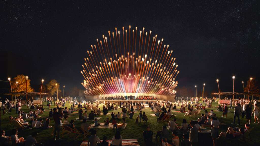 A half-shell performance pavilion constructed from illuminated vertical posts on a lawn at night.