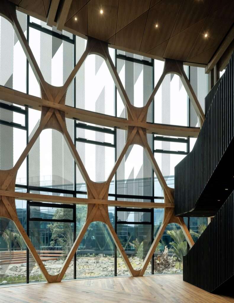 Double-height interior space showing an intricate mass-timber diagrid frame along a curtain wall.