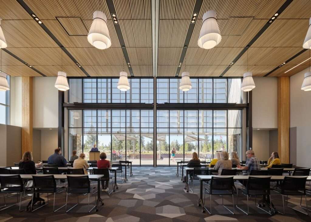 Large meeting room with rows of tables and chairs facing a floor-to-ceiling glass wall.