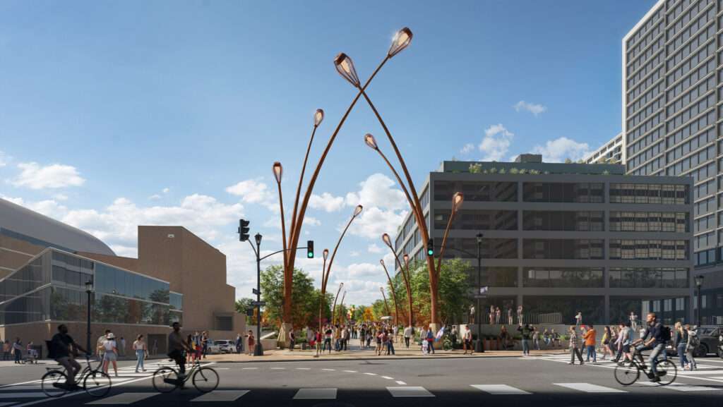 Pedestrian crosswalk leading to a park entrance framed by tall, arching lampposts.
