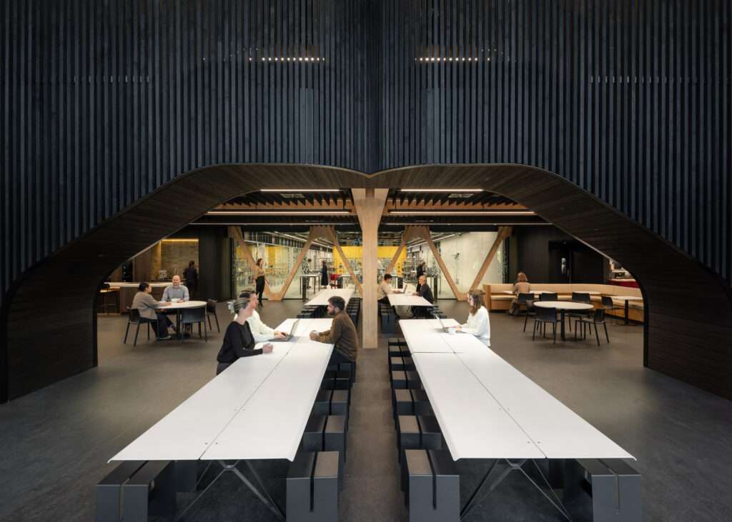 Symmetrical interior shot of a long dining area with white communal tables framed by dark timber soffits.