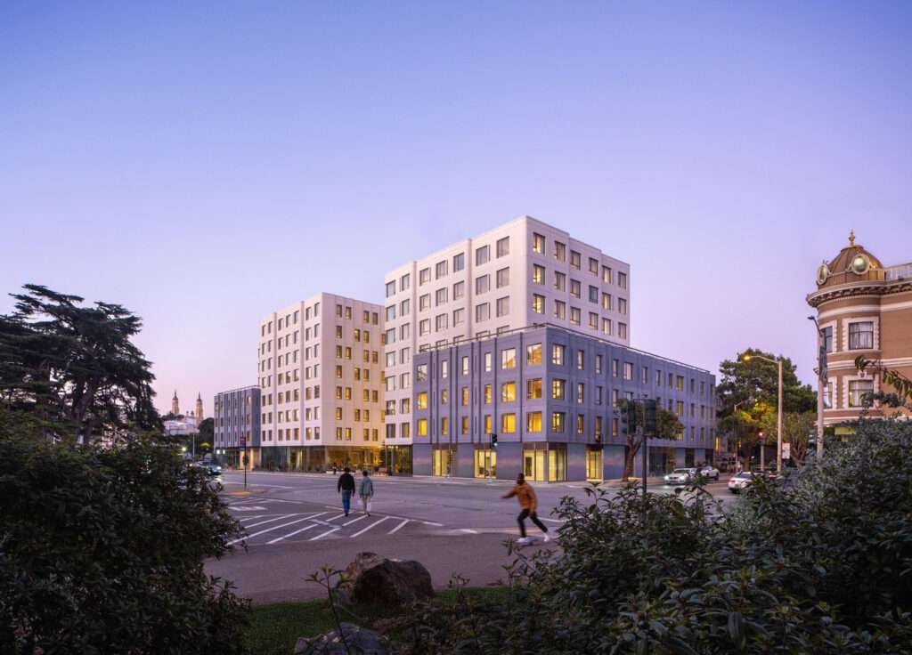 Street corner view at twilight showing illuminated windows, upper massing, and surrounding intersection.