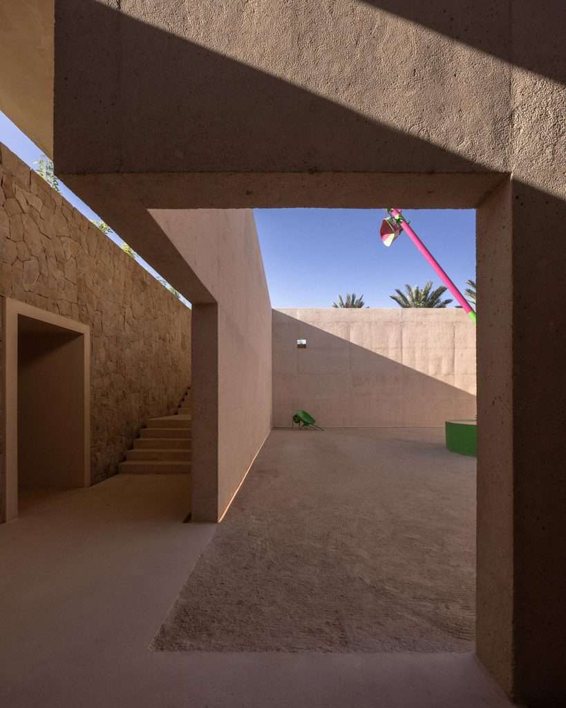 View from a shaded concrete corridor looking out towards a sandy courtyard and stone wall staircase.