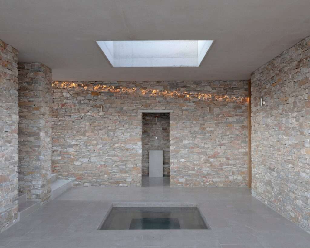 Enclosed stone hall with a square recessed floor pool beneath a rectangular ceiling skylight.