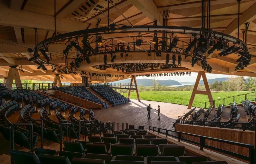Tiered seating bowl facing a wooden stage framed by A-frame timber supports and distant mountains.