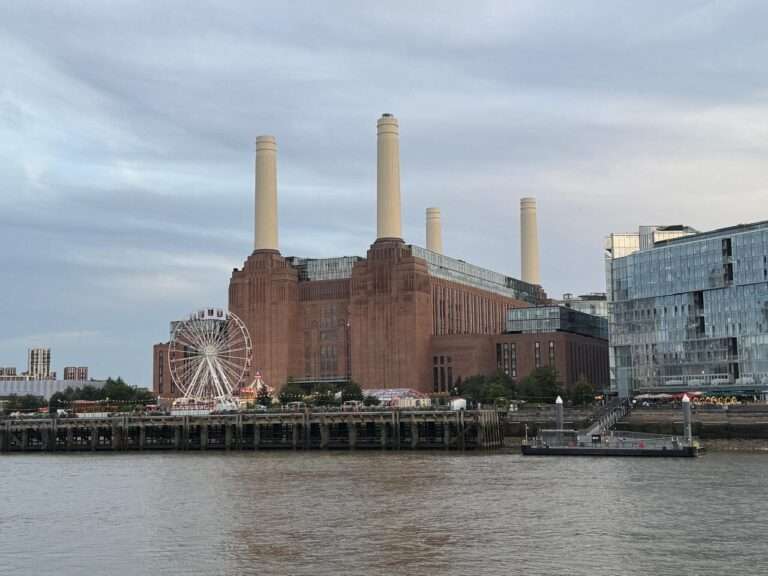 Battersea Power Station seen across the River Thames, with an illuminated Ferris wheel on the waterfront