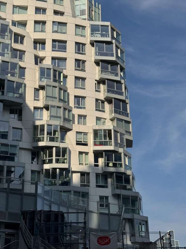 منظر تفصيلي من زاوية متوسطة للواجهة البيضاء النحتية لـ (Prospect Place). الشبكة الإنشائية (الإنشائية) الأساسية مشوهة بشكل مرئي لتتخذ أشكالاً عضوية تشبه الأمواج، مما يوضح كيف يحقن (يُدخل) جيري حركة ديناميكية في إطار سكني قياسي.