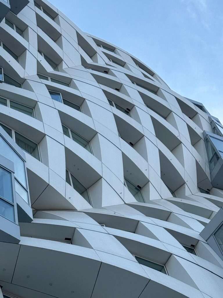 لقطة قريبة ومدهشة لواجهة جيري البيضاء، تُظهر بوضوح التوتر المعماري بين شبكة النوافذ العقلانية الموحدة والأشكال الخارجية البيضاء المعبرة، الجاذبة والمتموجة التي تحدد هوية مشروع (Prospect Place).