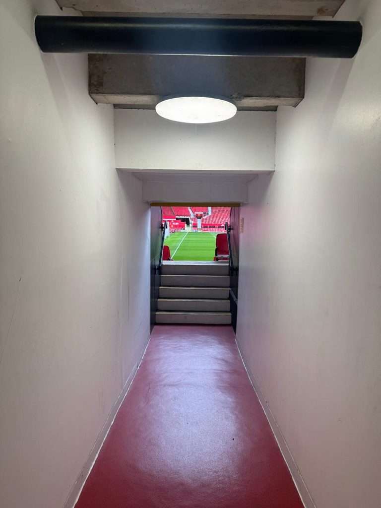 View from inside a players' tunnel looking out onto a green football pitch and red stadium stands