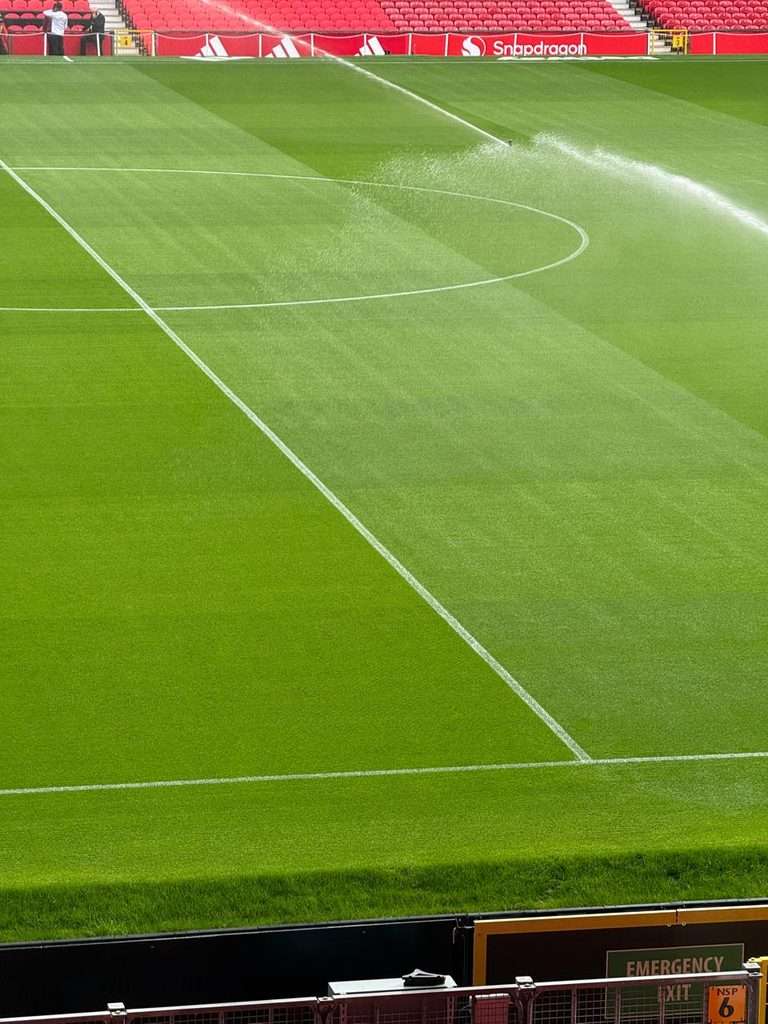 Water sprinklers spraying across a green football pitch in a stadium