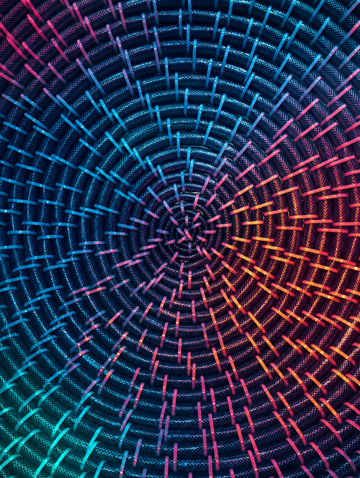 An abstract, mesmerizing spiral pattern made of coiled dark textured cables secured by small structural ties, illuminated by a vibrant neon gradient of cyan, magenta, and orange lighting.