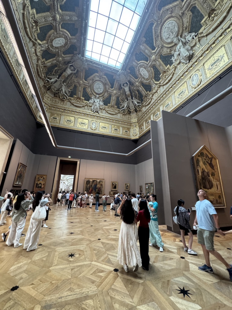 The historic Salon Carré in the Denon Wing of the Louvre Museum, with its magnificent gilded ceiling and collection of early Italian Renaissance paintings including Giotto's Saint Francis of Assisi Receiving the Stigmata.