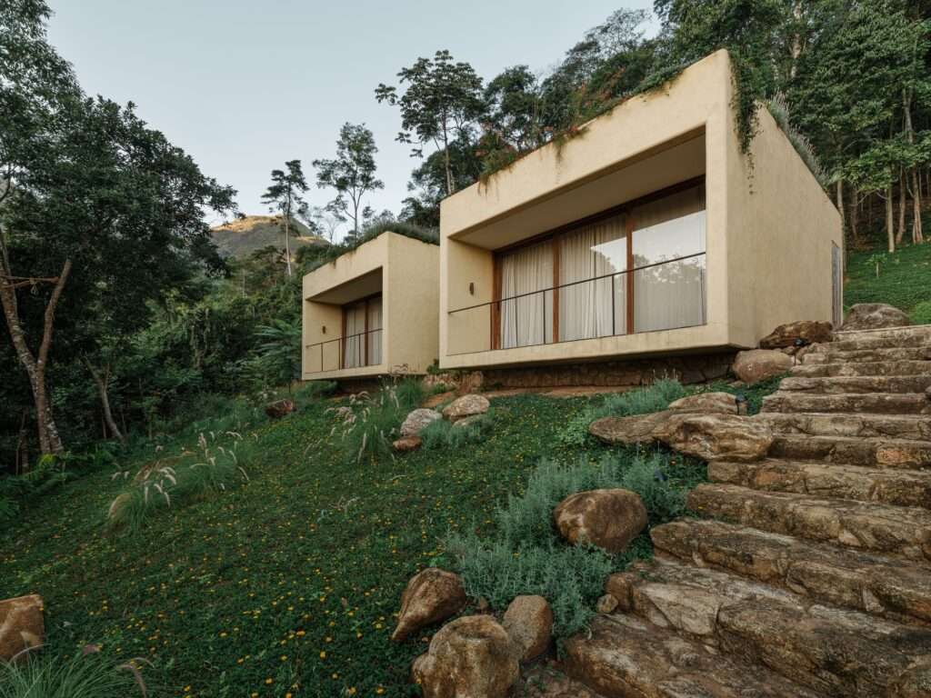 Exterior view of concrete suite volumes with green roofs nestled into a grassy mountain slope at Japú House by AIA Estúdio.