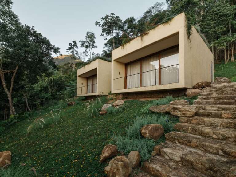 Exterior view of concrete suite volumes with green roofs nestled into a grassy mountain slope at Japú House by AIA Estúdio.