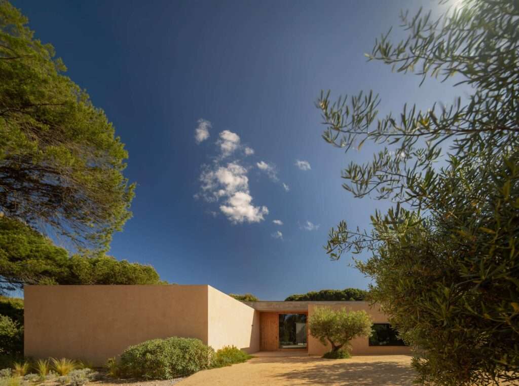 Earth-toned exterior wall of Muda L13 House surrounded by pine trees and natural landscape in Grândola.