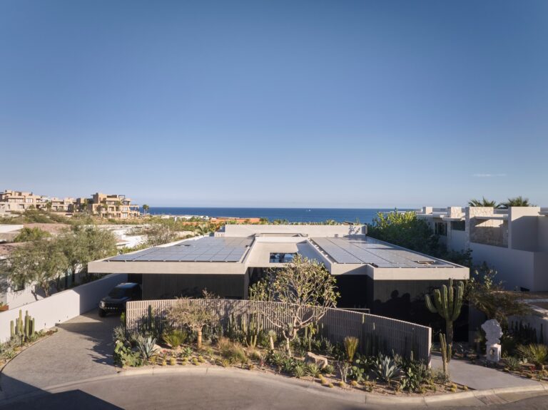 Aerial view of Casa Loto featuring solar roof panels and dark concrete volumes overlooking the sea horizon in Los Cabos.