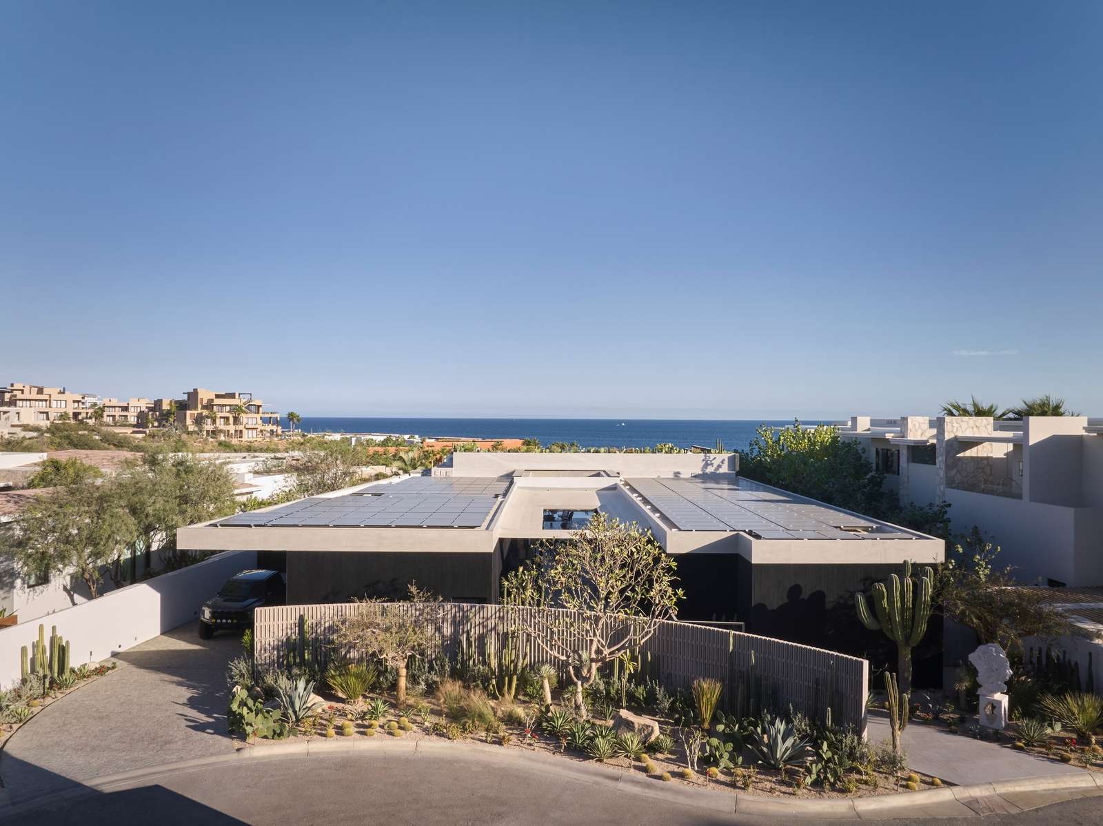 Aerial view of Casa Loto featuring solar roof panels and dark concrete volumes overlooking the sea horizon in Los Cabos.