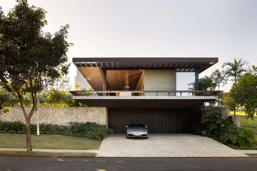Front elevation of Casa da Mata featuring a floating roof canopy with a slatted wooden ceiling, raw fieldstone retaining wall, and a garage with a parked sports car.