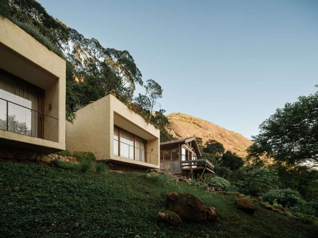 Side perspective of Japú House showing concrete bedroom blocks and gabled wooden pavilion aligned along mountain contour lines.