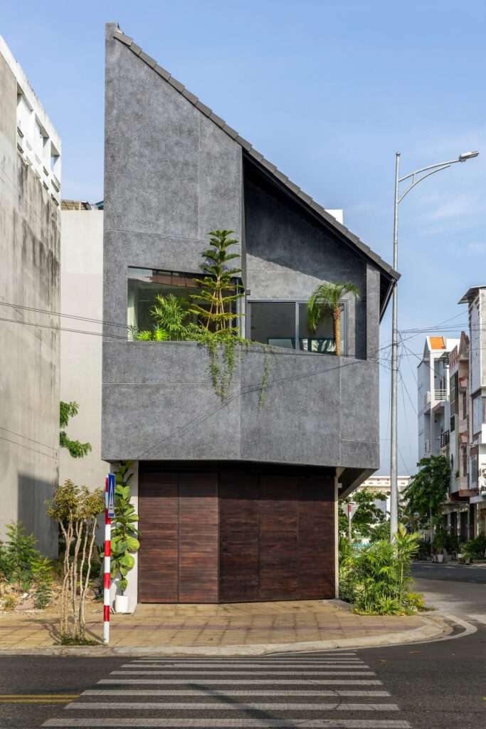 Front elevation of the Inner Courtyard House showing the angled textured concrete upper level with embedded planter balcony above a dark timber garage entrance gate.