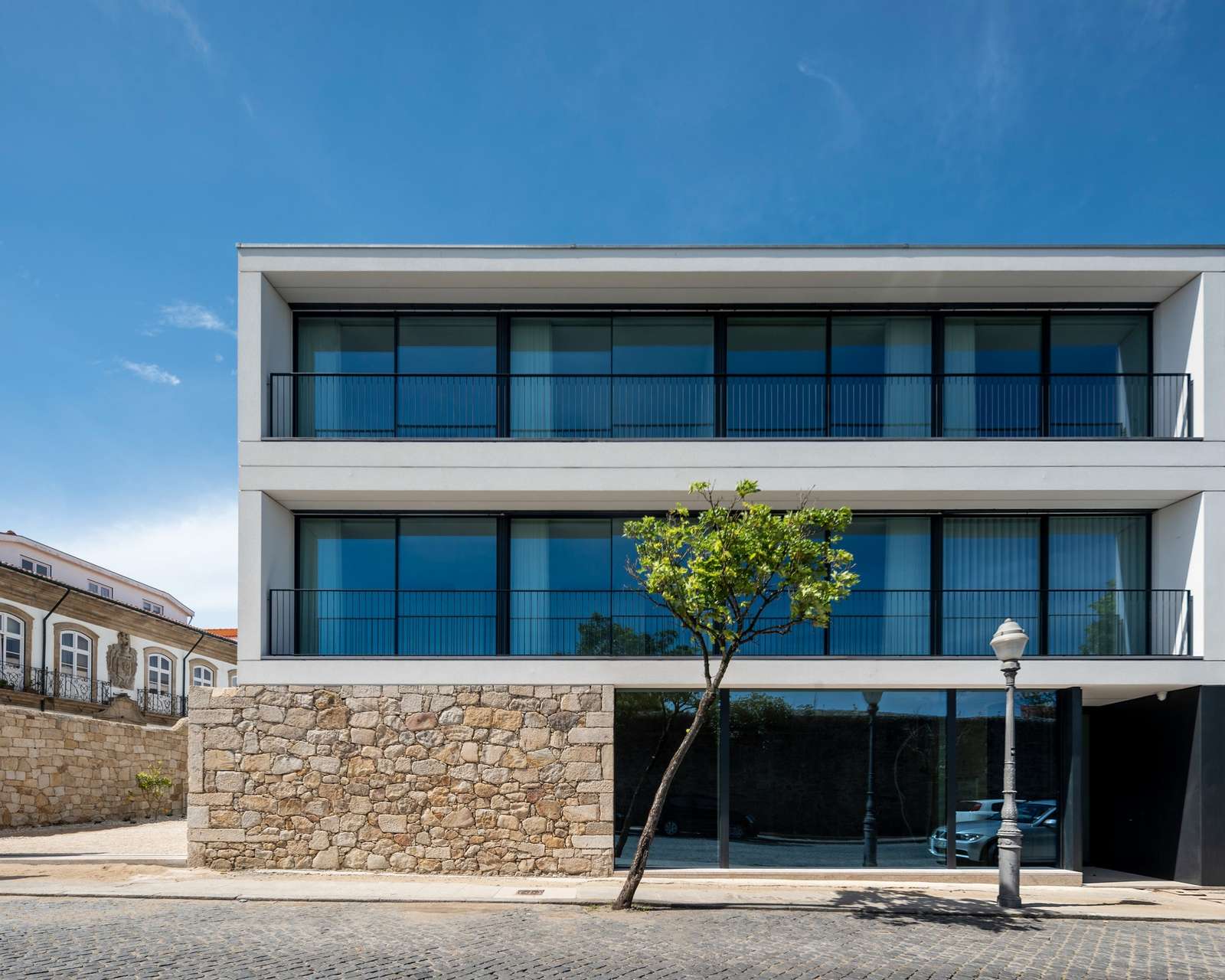 Modern white residential building with large glazed balconies built above an ancient stone wall base in Vila do Conde.