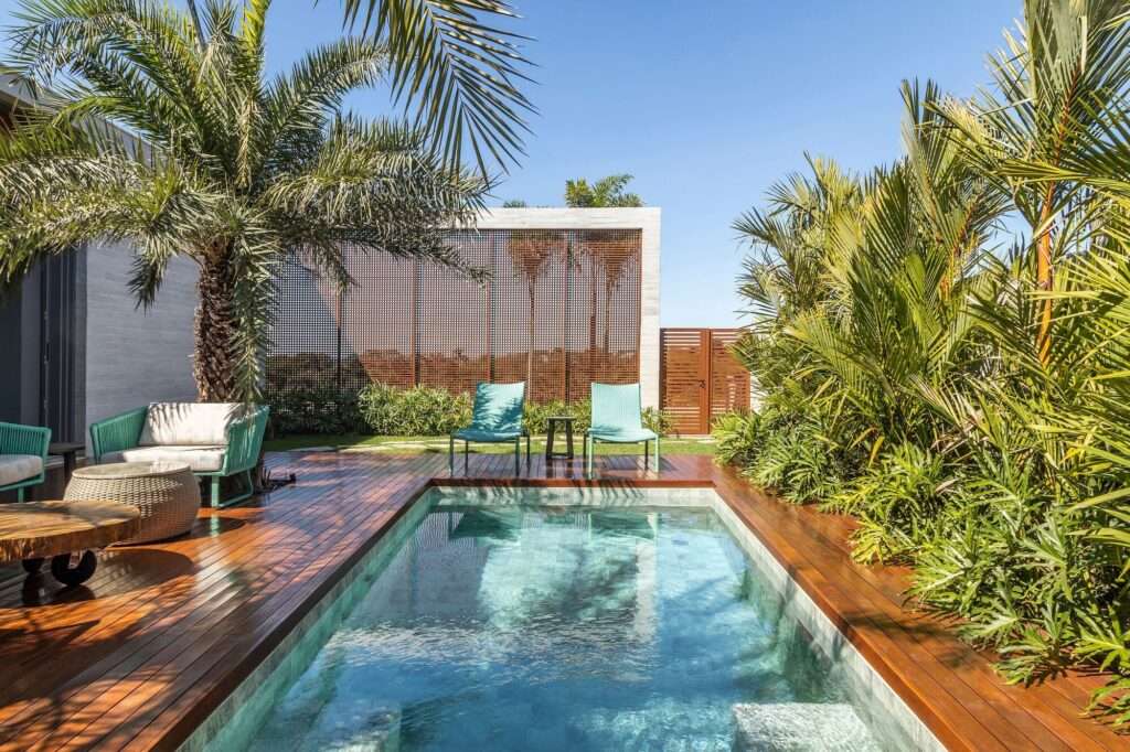Outdoor swimming pool area surrounded by wooden decking, sun loungers, palm trees, and mashrabiya privacy screens.