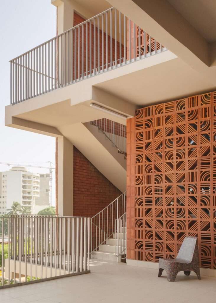 Detailed view of patterned terracotta clay brick mashrabiya screen framing an outdoor staircase and balcony area.