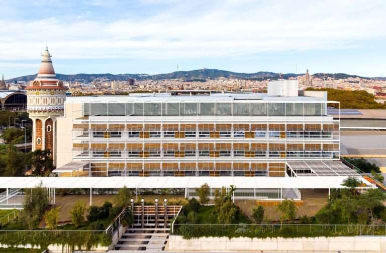 Front elevation of Hospital del Mar expansion showing modular louvered facade, green rooftop garden, and historic water tower in Barcelona.