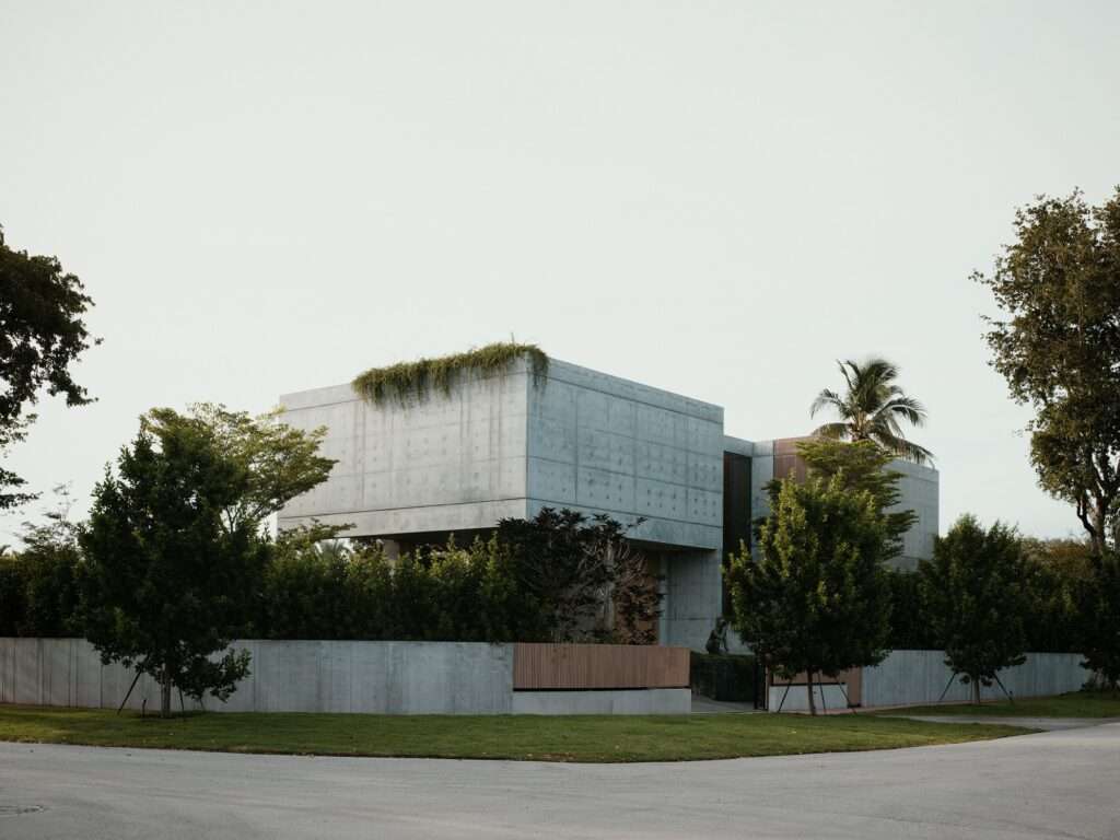 Exterior street view of Cherokee House showing two cast-in-place concrete volumes with cantilevered overhangs and surrounding green foliage.