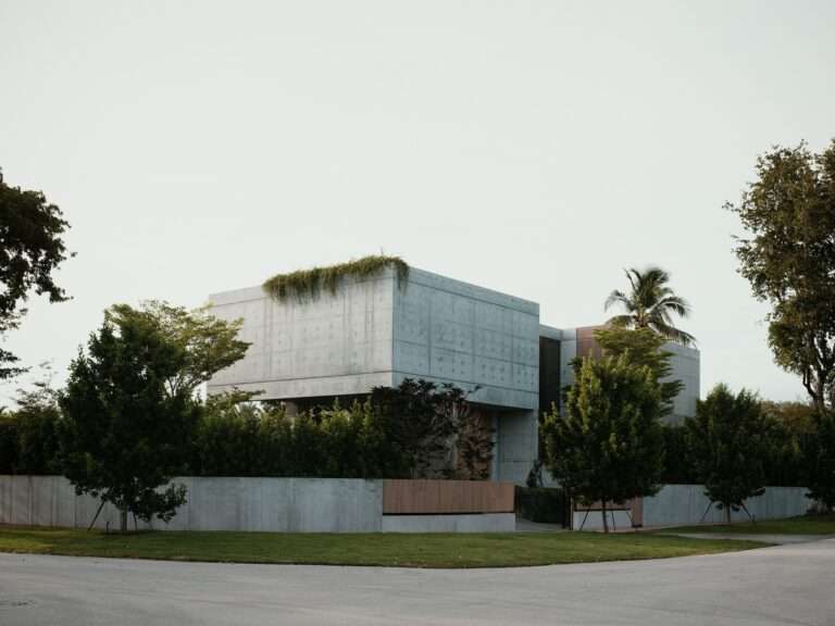 Exterior street view of Cherokee House showing two cast-in-place concrete volumes with cantilevered overhangs and surrounding green foliage.