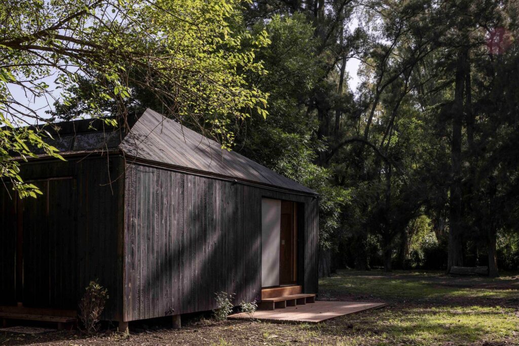 Exterior shot of Etchegoyen House showing dark charred wood vertical cladding, low-pitched roof, and small wooden entrance platform.